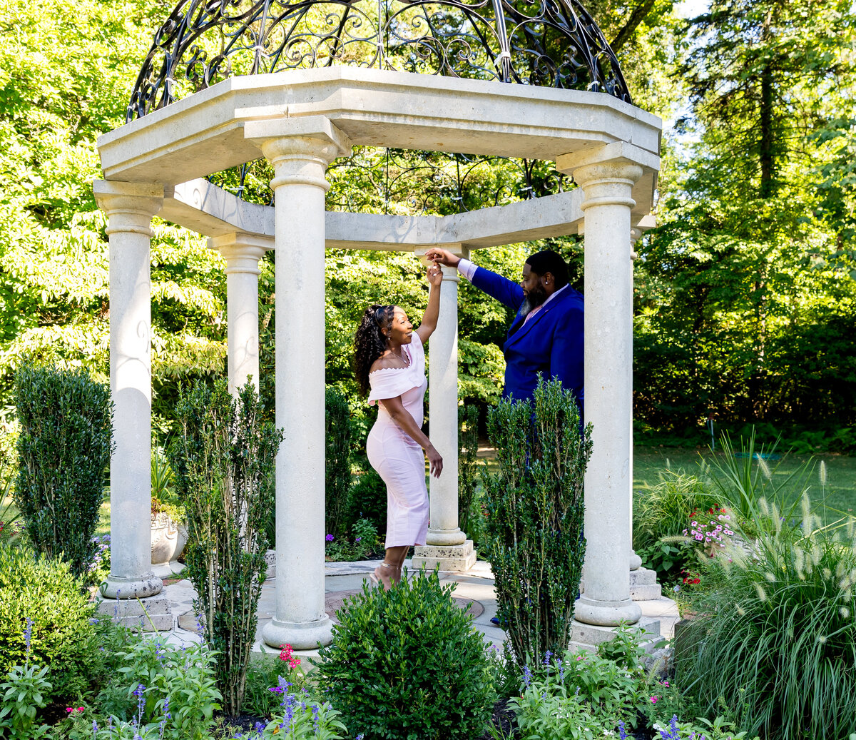 The young black couple is dancing in a garden for their engagements pictures. The day is sunny and clear skies.