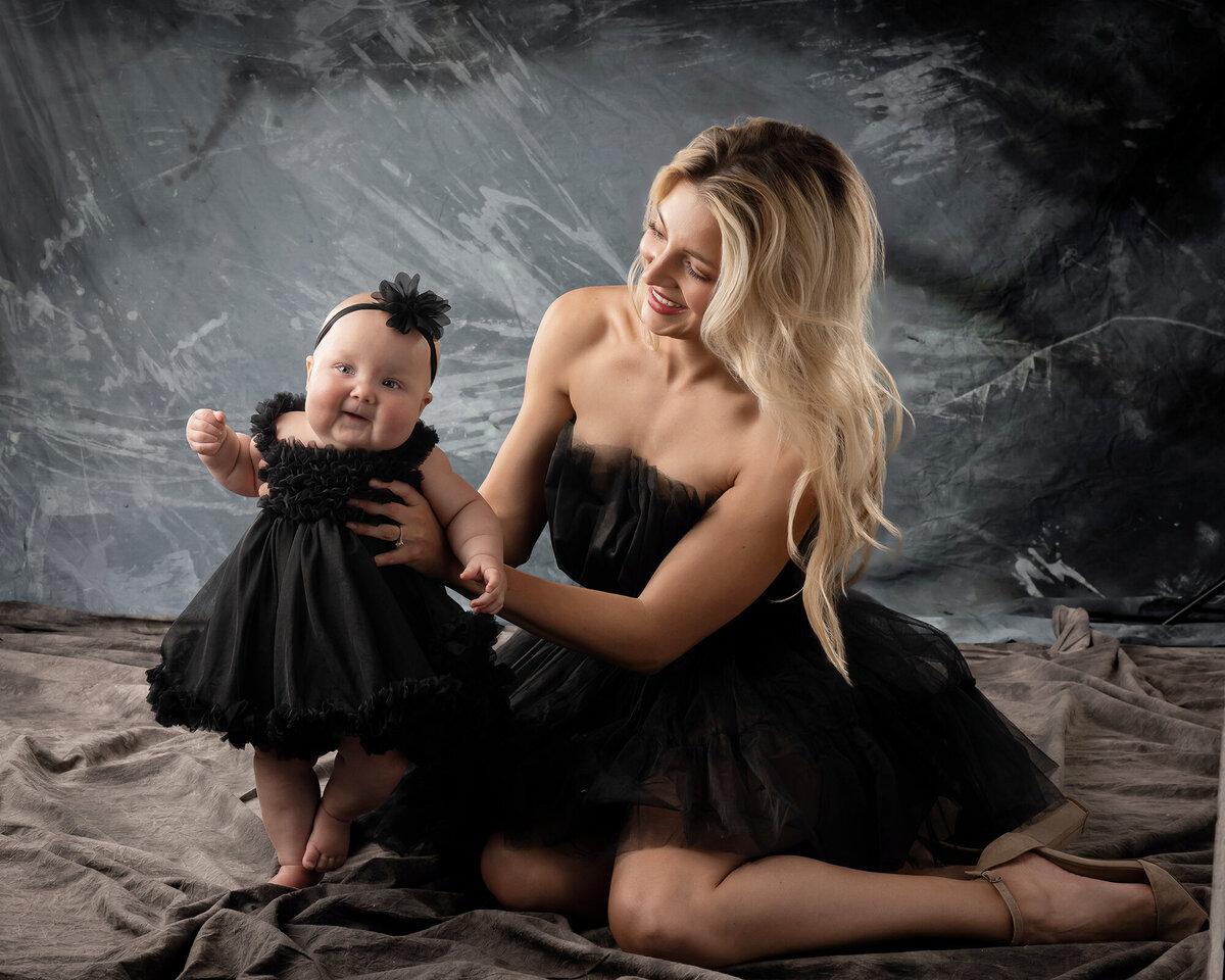 Mom looks at daughter smiling while helping her stand for their Des Moines Family Portraits