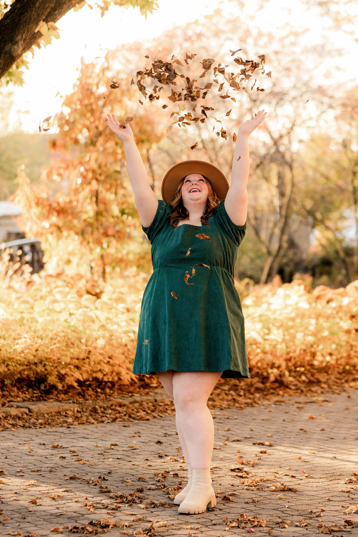 a high school senior  girl throws leaves into the air while laughing.