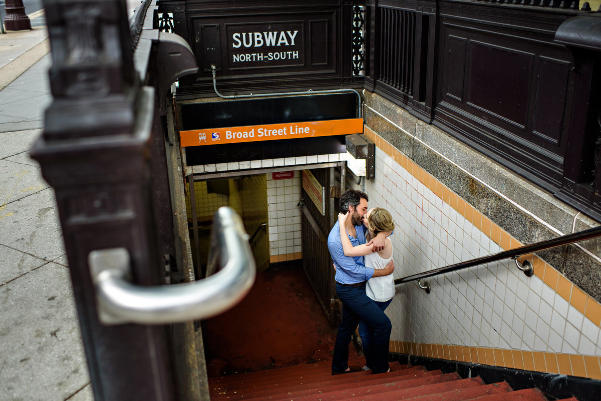 Coming out of the philly subway, a couple stop on the stairs for a kiss.