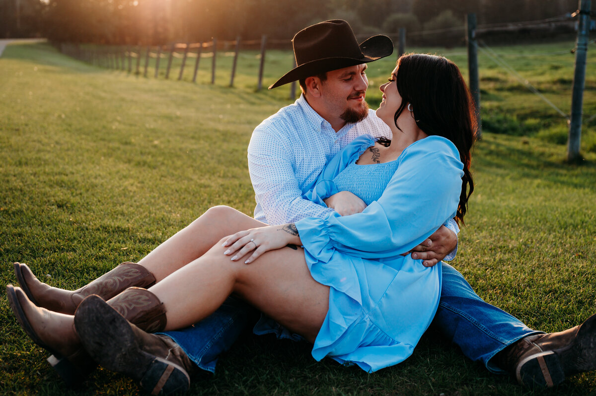 couple sits in the middle of a field near Edmonton, Alberta looking at each other, while golden sun shines in the background