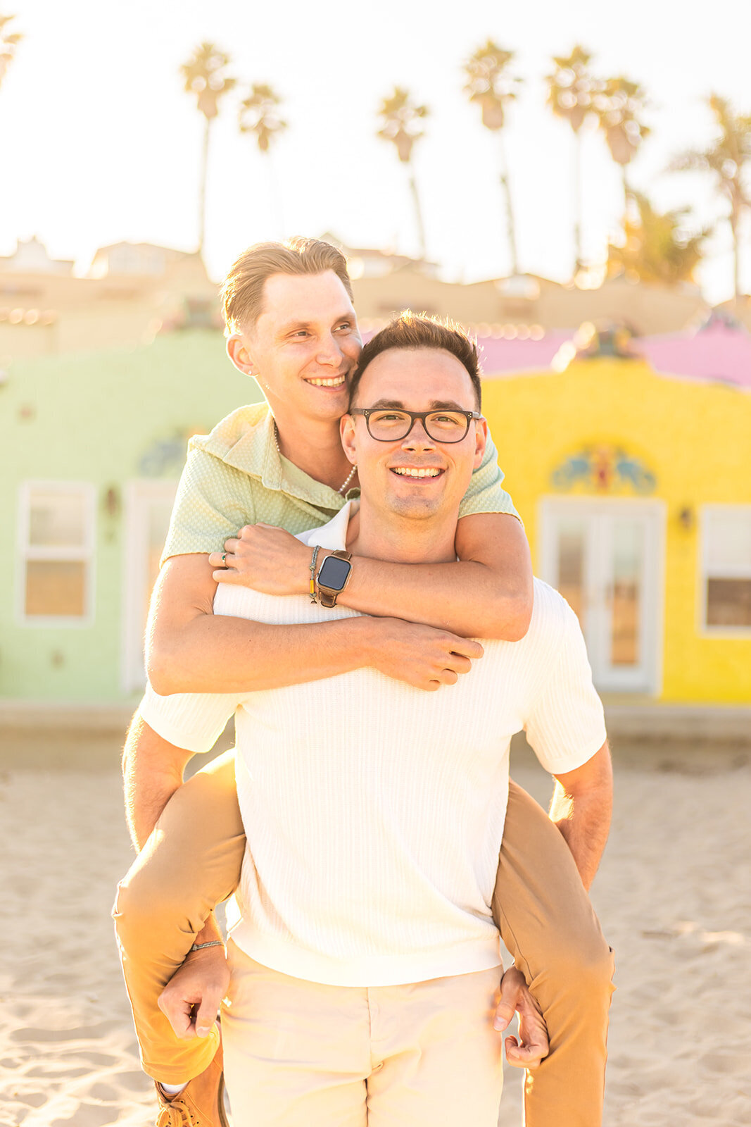 gay couple with two grooms piggyback ride on beach