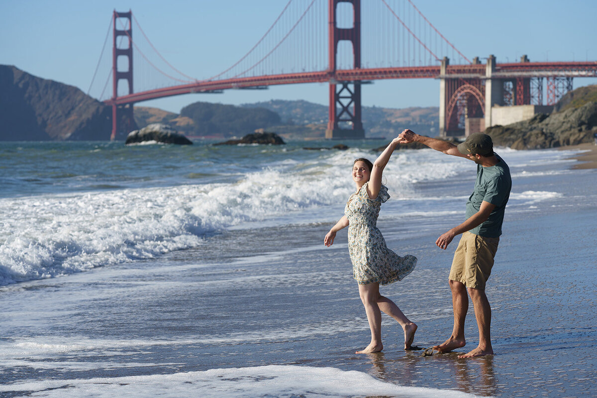 Couple dancing on the beach in the surf with the golden gate bridge in the background