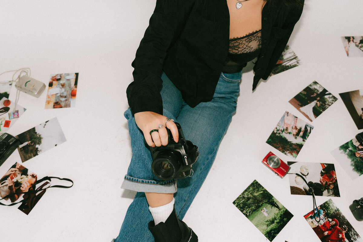 Documentary wedding photographer holding canon camera, surrounded by wedding photographs and cameras