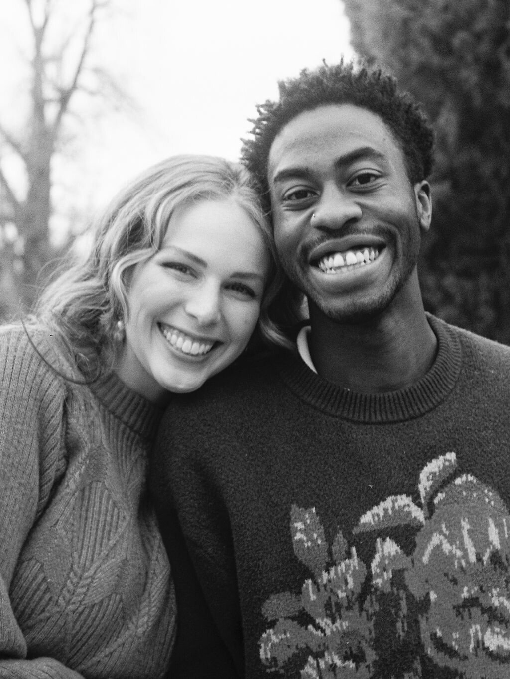 A couple smiles at the camera with their heads pressed close together during their engagement photos.