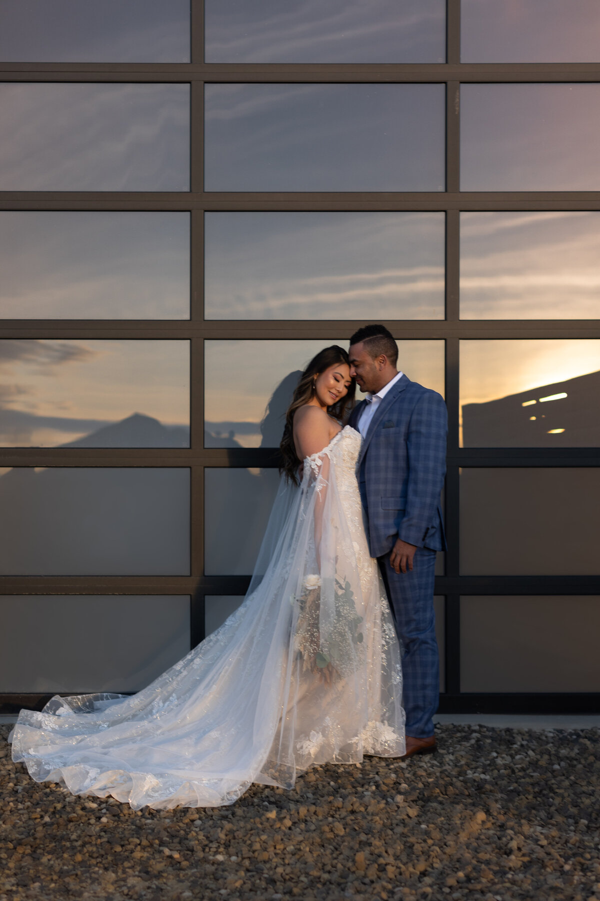 She's facing camera and he's looking at her in front of white barn glass door with incredible sunset reflection.
