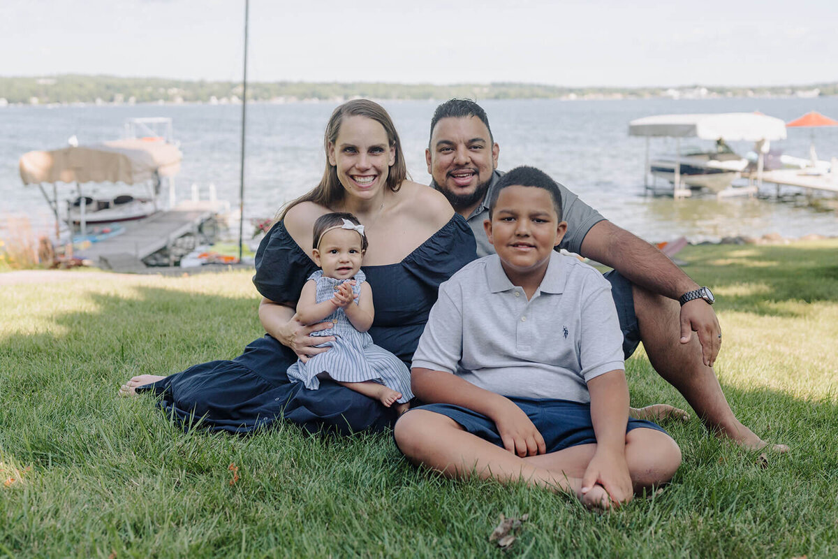 Family with two kids sitting on grass overlooking lake at generational photoshoot in Finger Lakes, NY