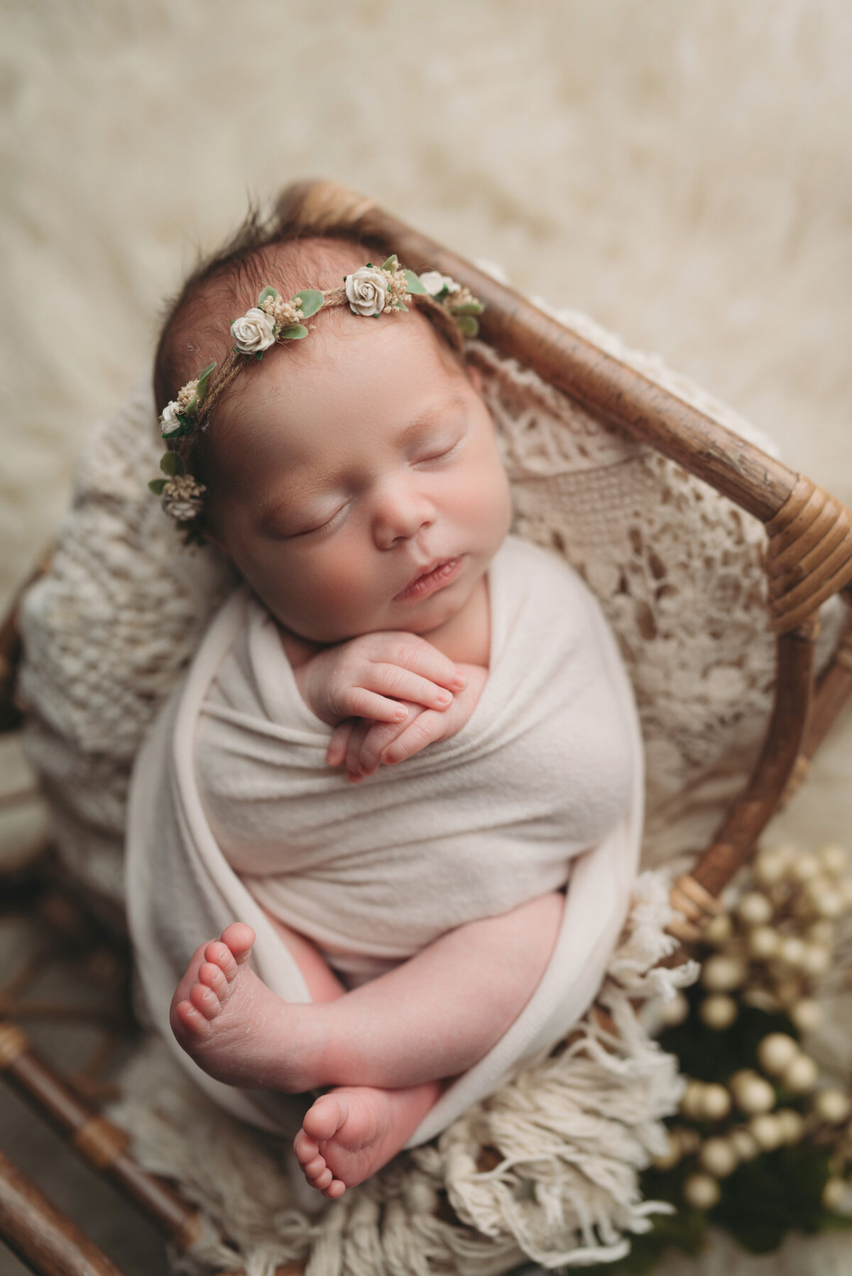 Newborn baby girl wrapped in  cream wrap  with feet and hands poking out laying in basket sleeping over boho layer and plant accent