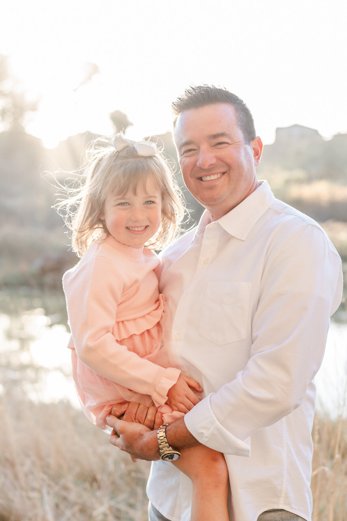 dad in a white shirt holding his little girl wearing a pink dress