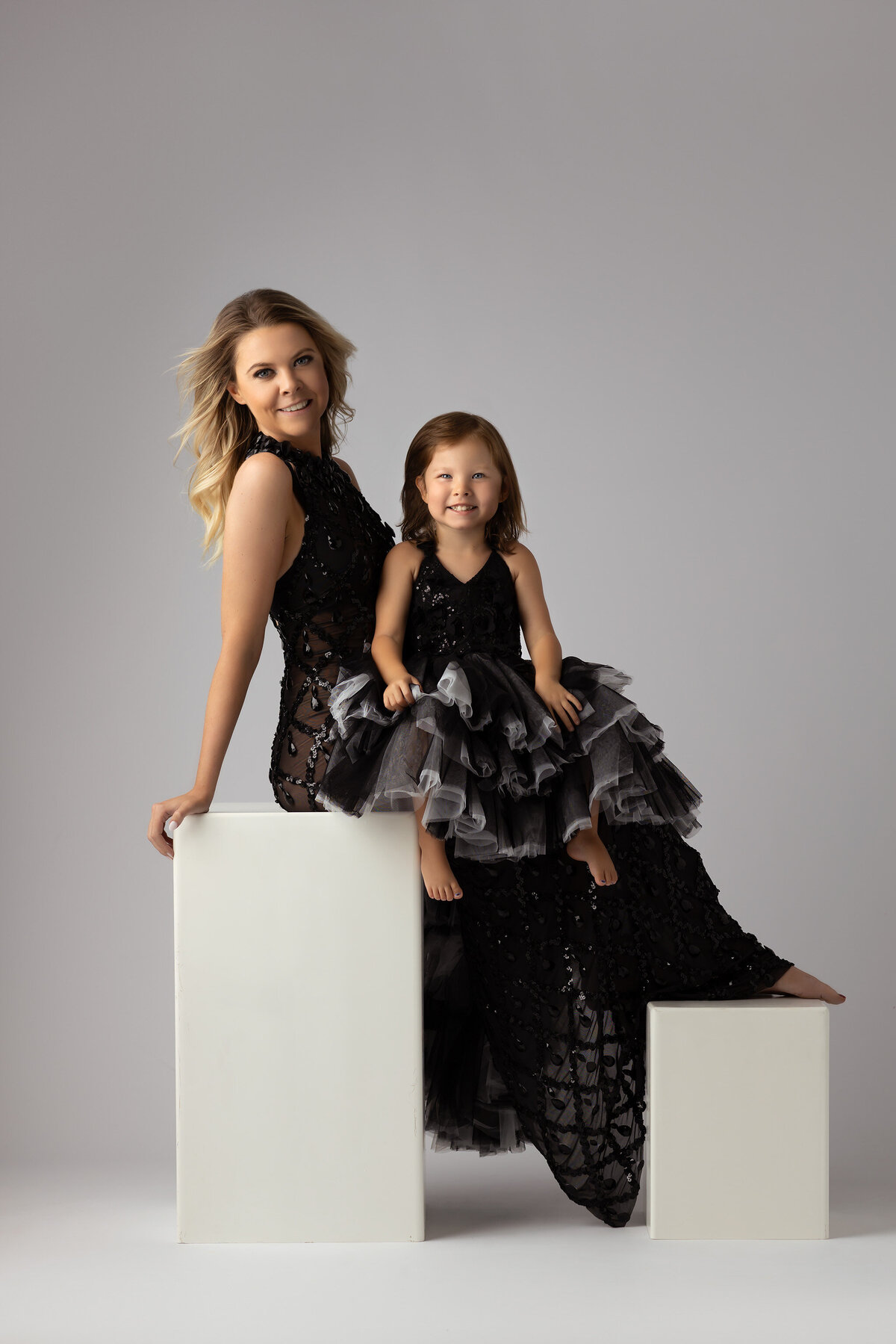 A stylish mother and daughter duo dressed in black dresses for a family photoshoot, captured by a Dallas family photographer in a simple, elegant studio setting.