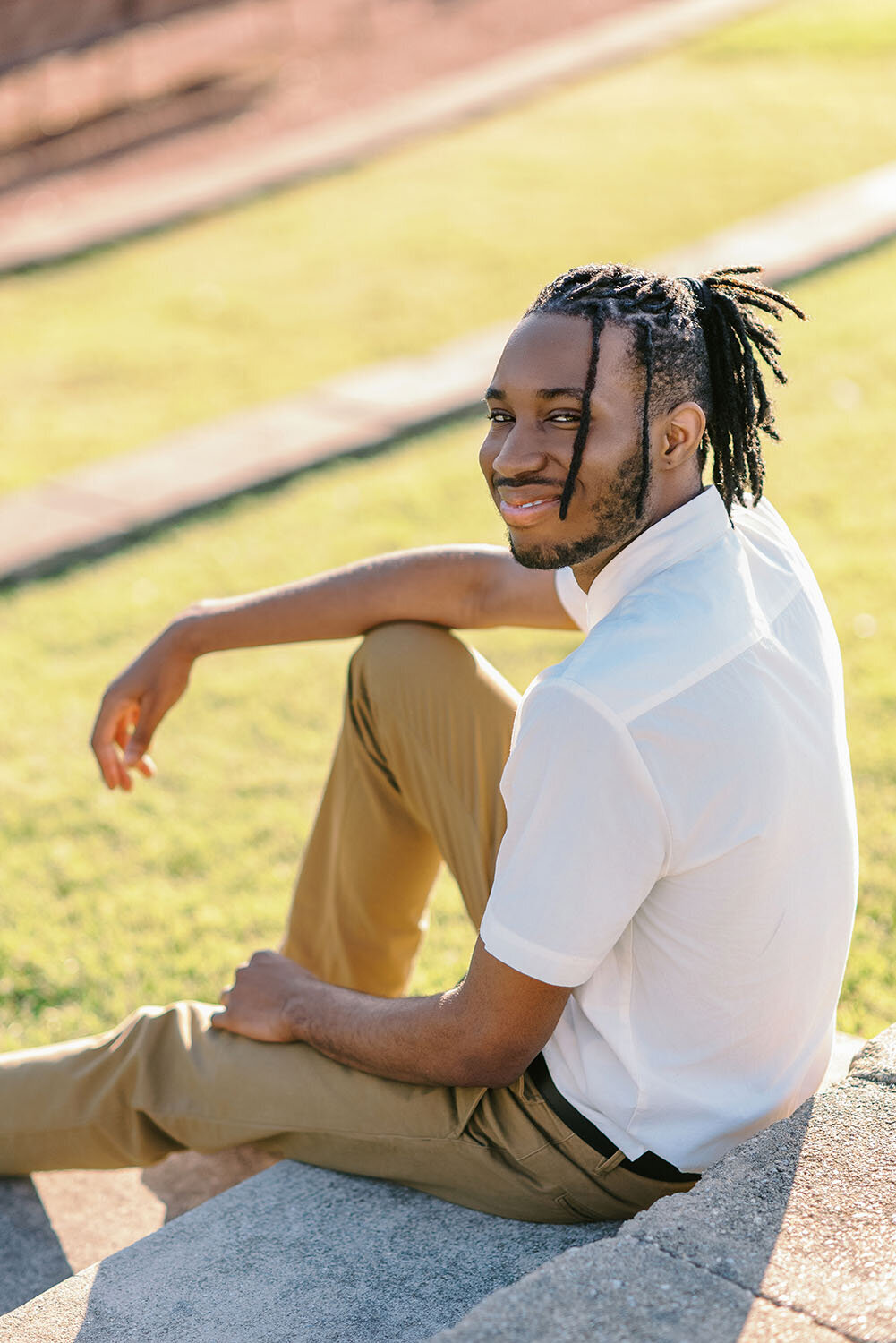 High school senior guy wearing a white shirt and khaki pants seated on steps at an outdoor amphitheater