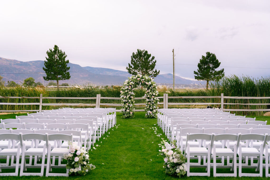 Outdoor ceremony seating facing a floral arch, with mountains beyond