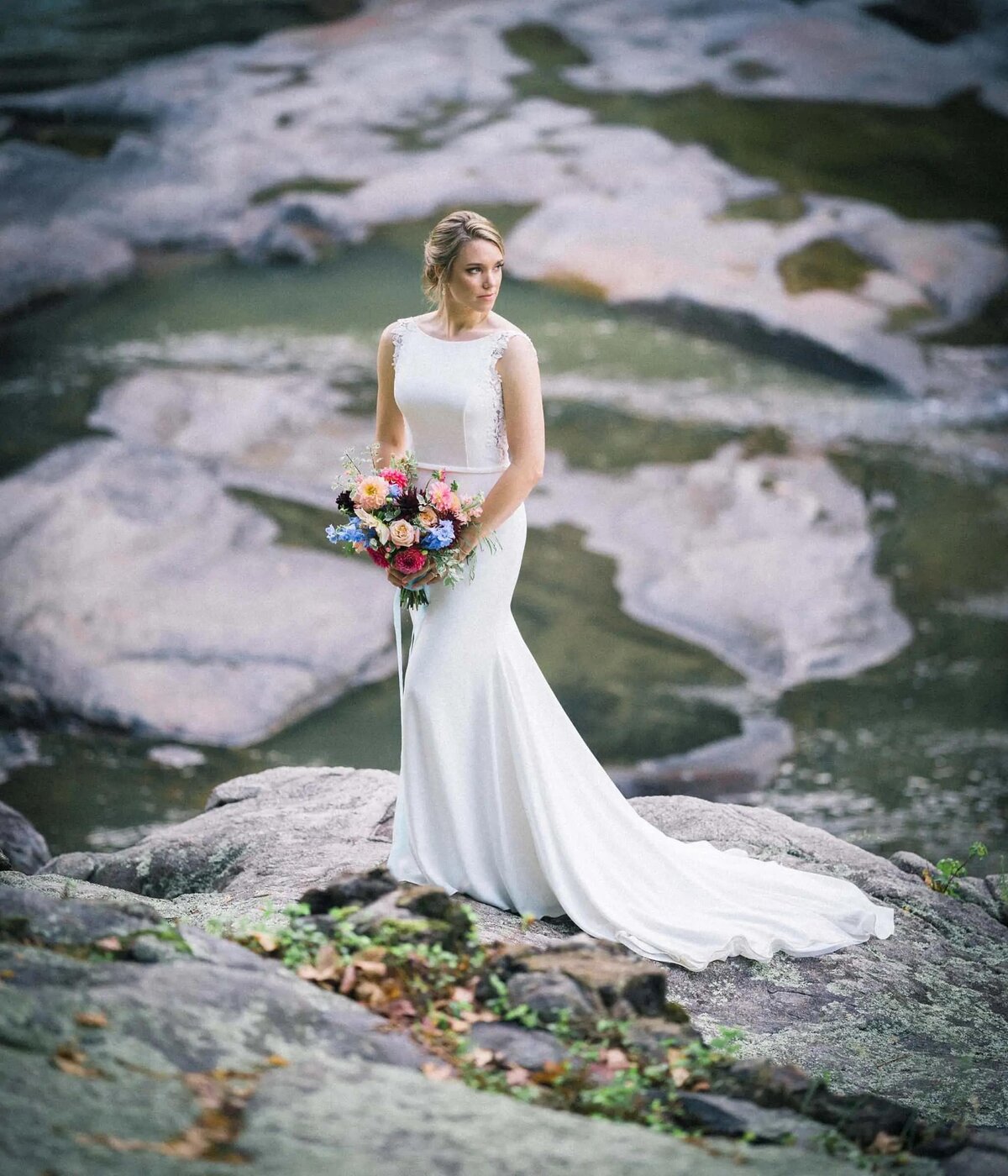 A bride smiling standing on a rocky overlook holding a bouquet