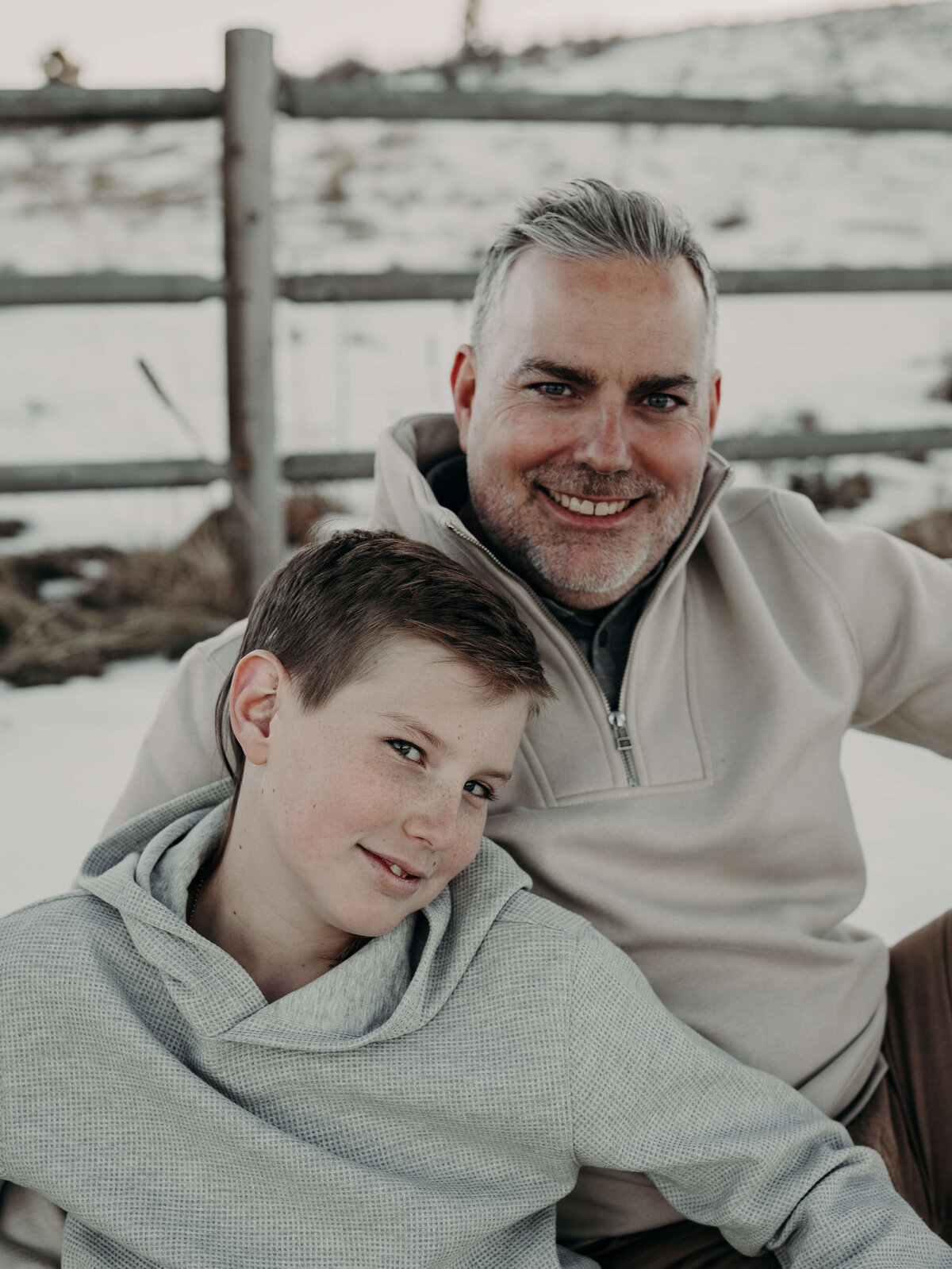 A father and son, wearing coordinating sweaters smile towards the audience during a family photo session during the winter in Denver, Colorado.