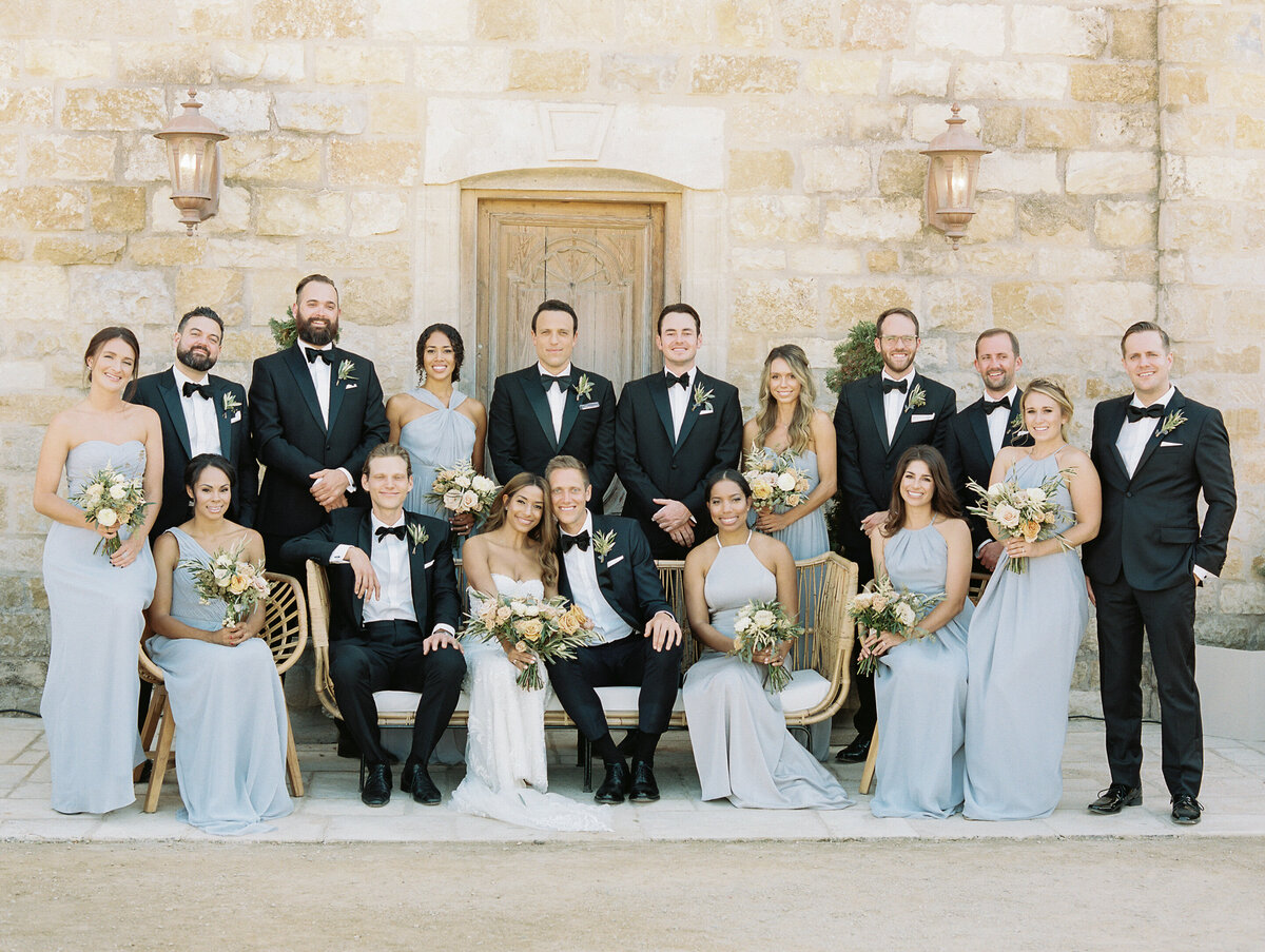 group photos of wedding party staged like a voque portrait with some sitting on bend and some standing. bridemiads wearing blue  gowns and groomsmen wearing black tuxes