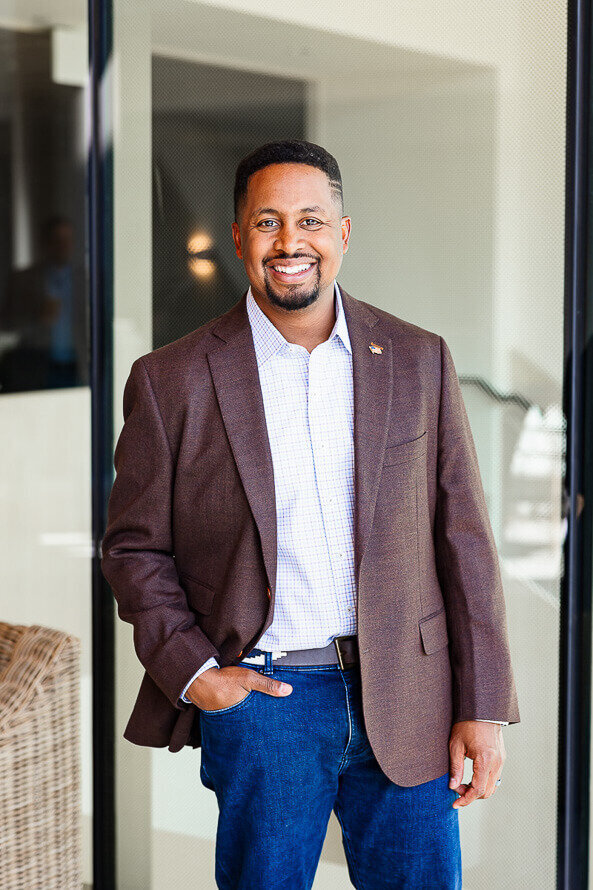 Man puts one hand in pocket  and smiles in a business setting.