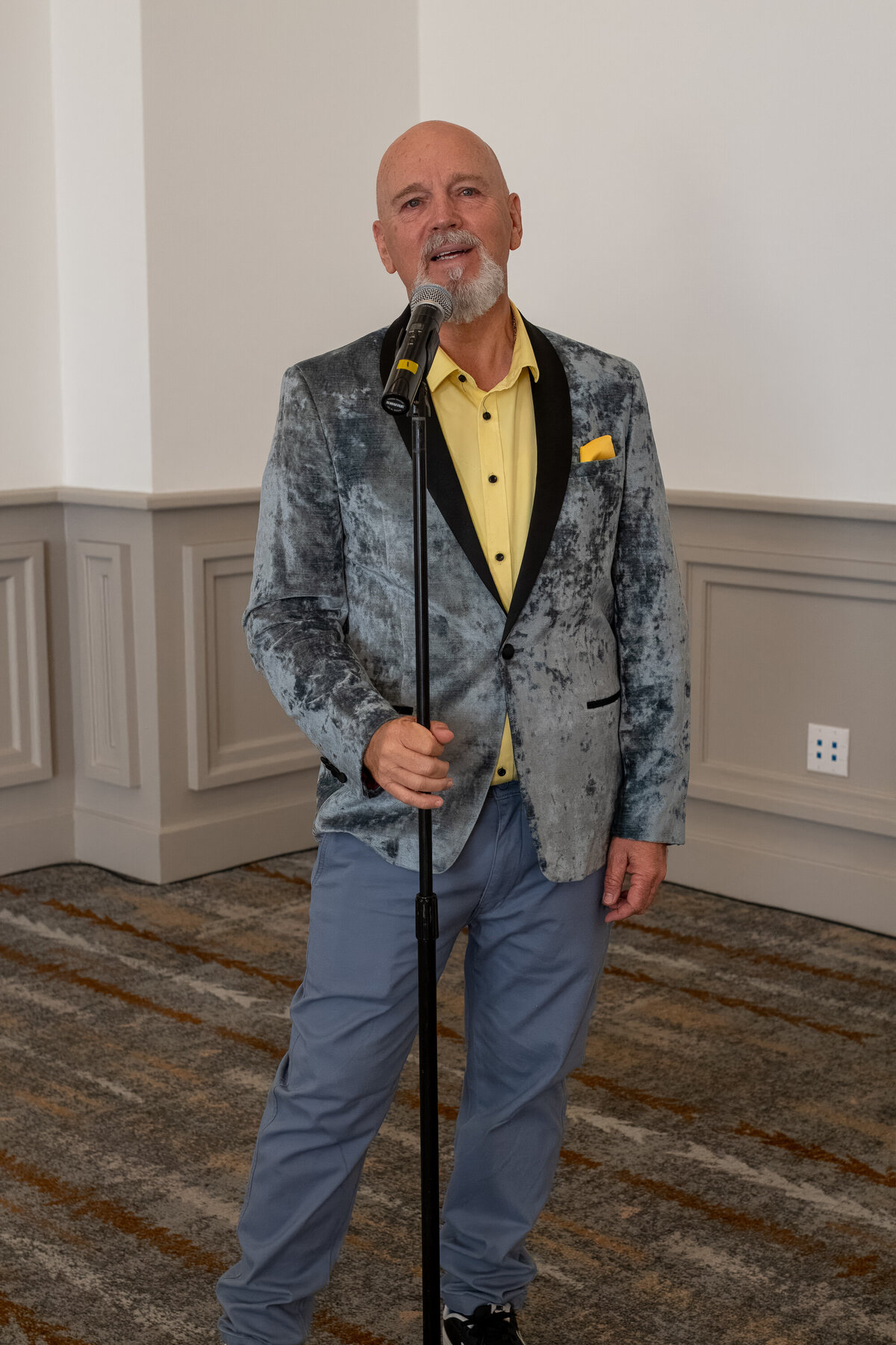 Man standing indoors with a microphone, wearing a patterned blazer and yellow shirt, photographed by Vyrl Photo, showcasing Tucson brand photography.