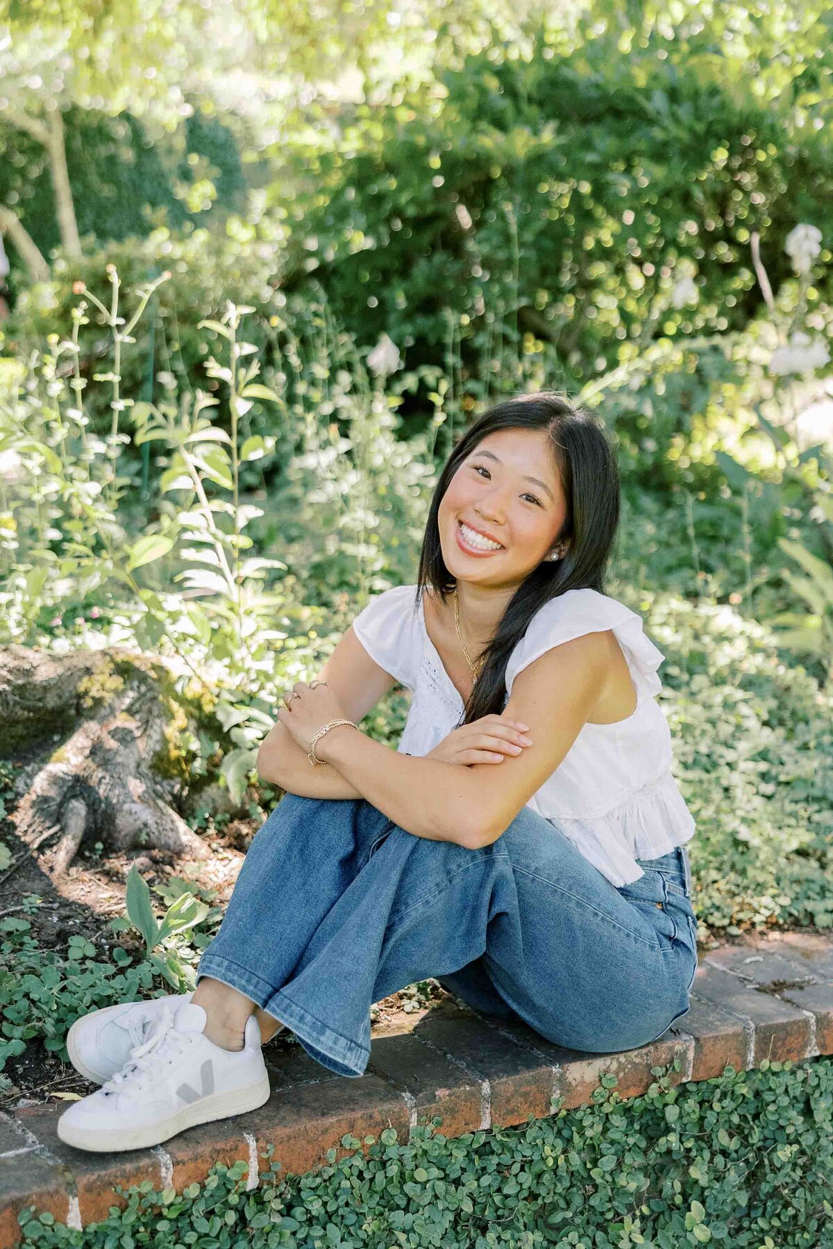 Asian girl smiling and sitting on a brick wall at Filoli Gardens in California