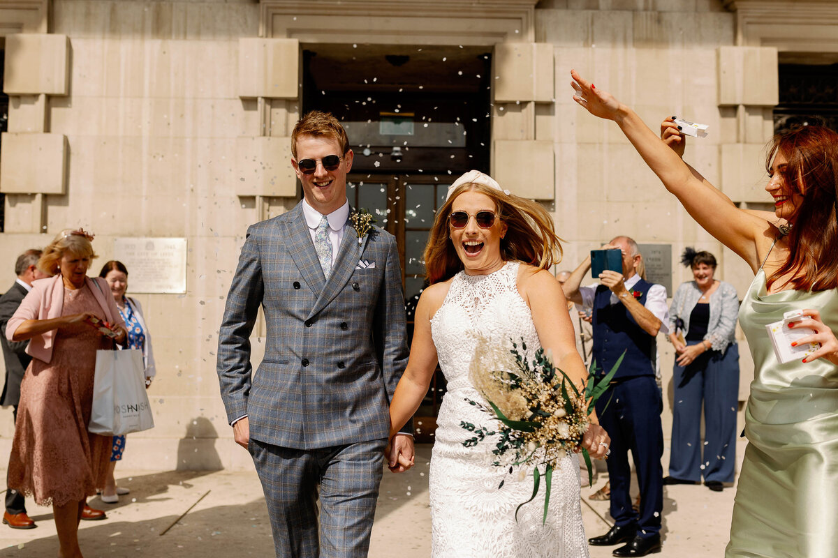 bride and groom wearing sunglasses exiting leeds civic hall to confetti