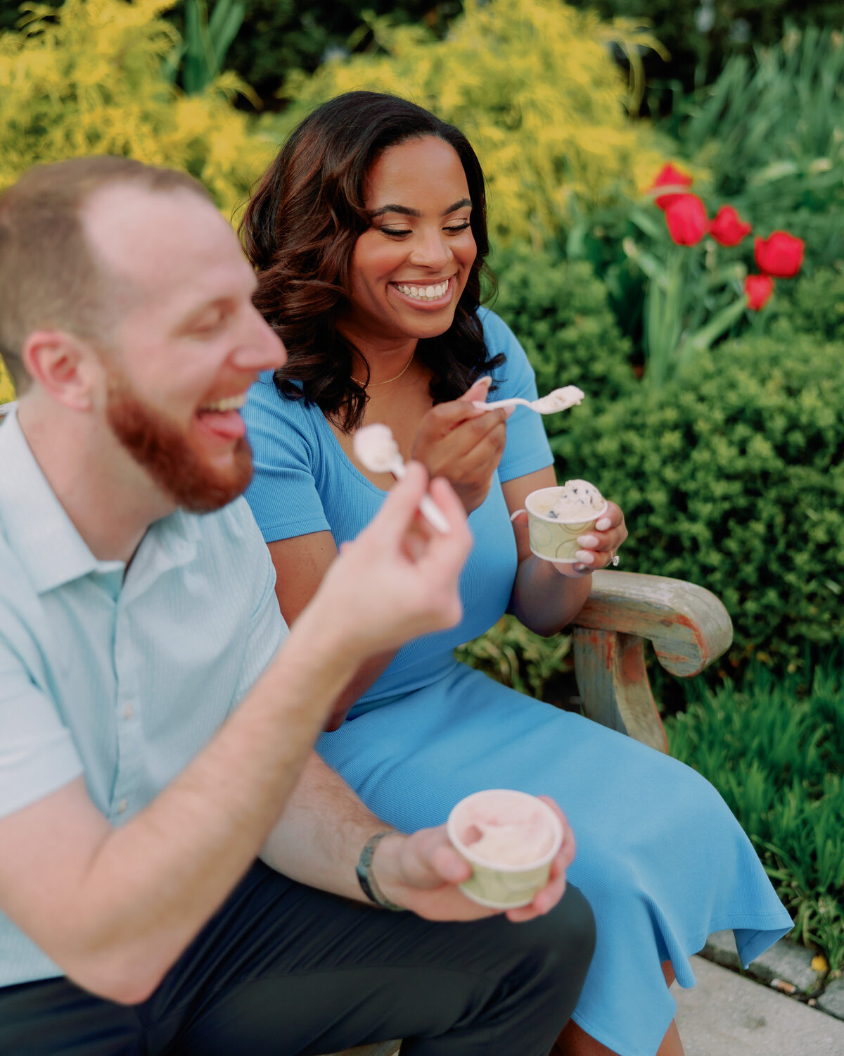 A couple laughing as they sit in a garden and eat ice cream 