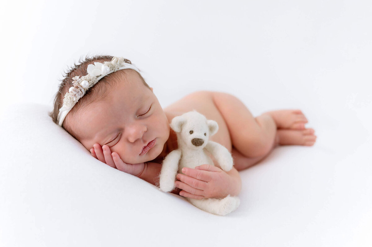 newborn baby girl laying on her side holding a tiny bear on a white background for her Burlington newborn photography session