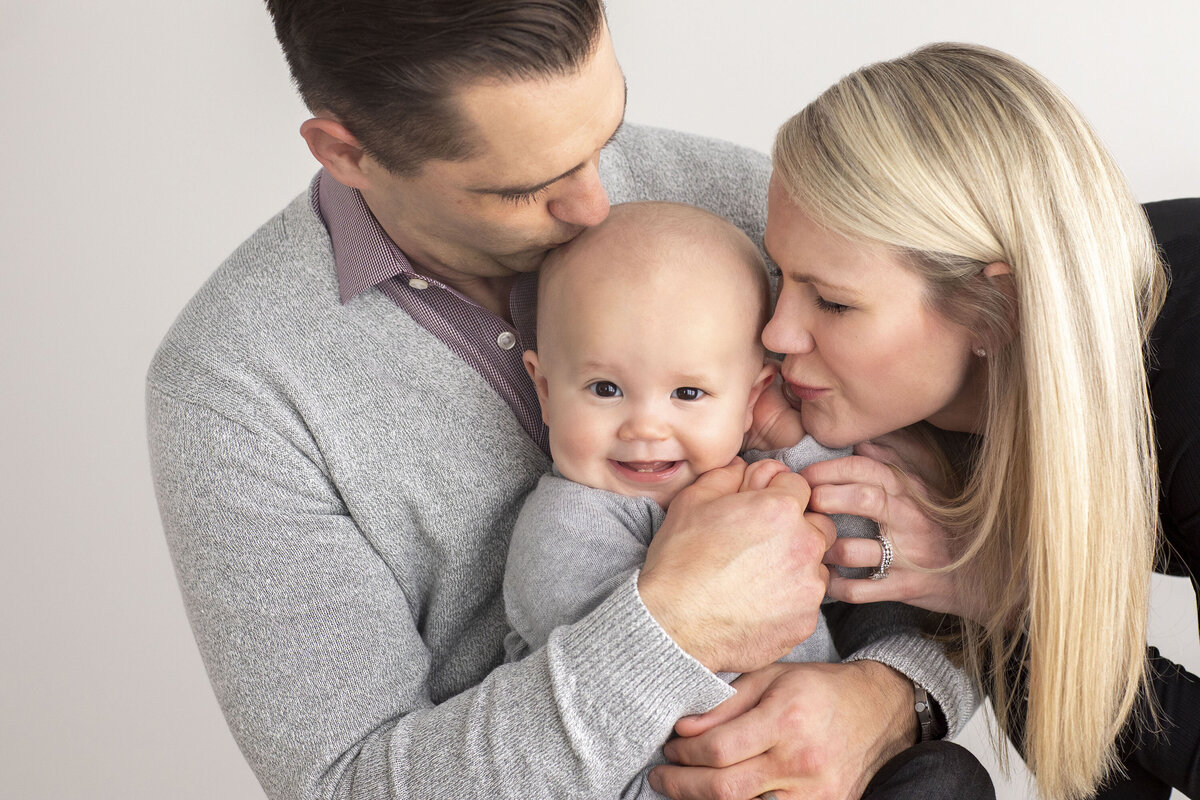 Mom and dad lovingly kissing their toddler on both cheeks, capturing a joyful and affectionate family moment during their photo session