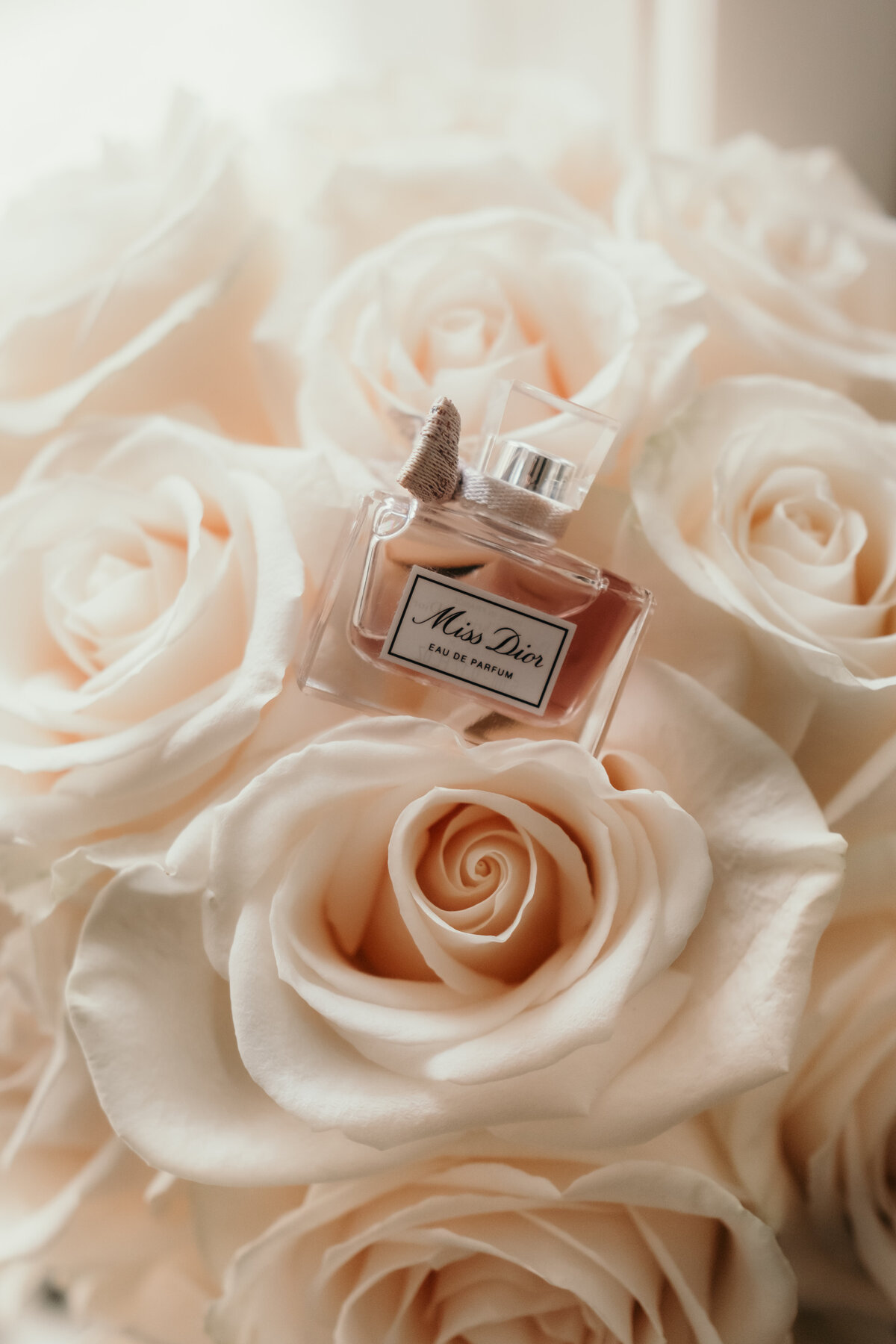 Detailshot of the brides parfum lying on beige roses.