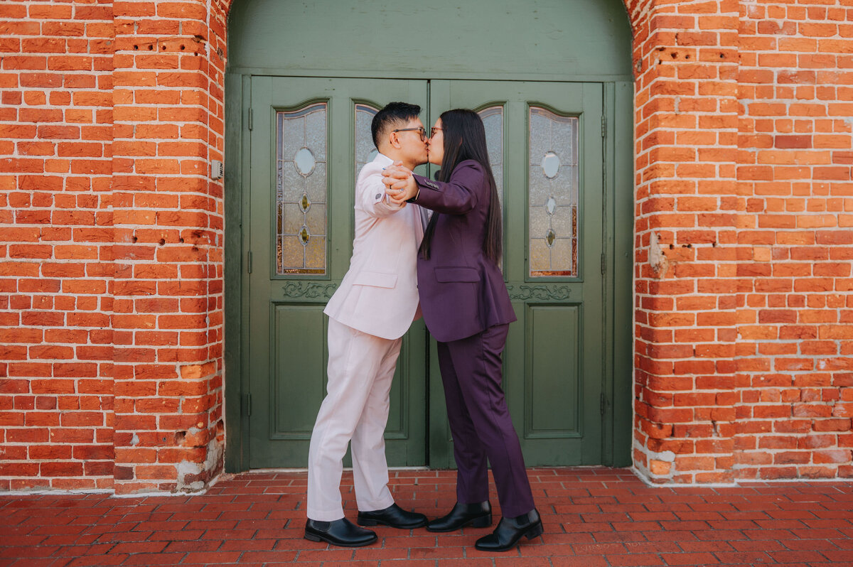 A couple leans in for a kiss in front of a green door