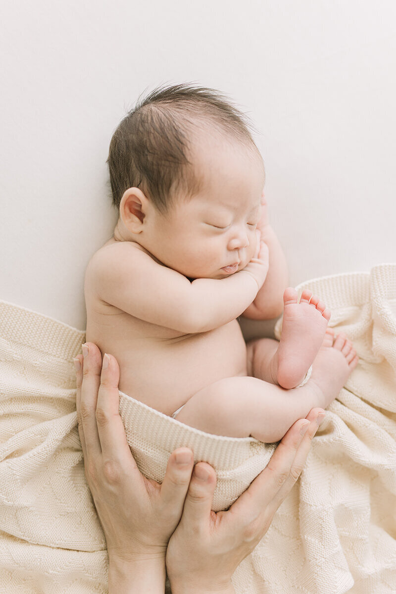 横向きで丸くなって寝ている赤ちゃんに、ママが手を添えているとても可愛らしくオシャレなニューボーンフォト