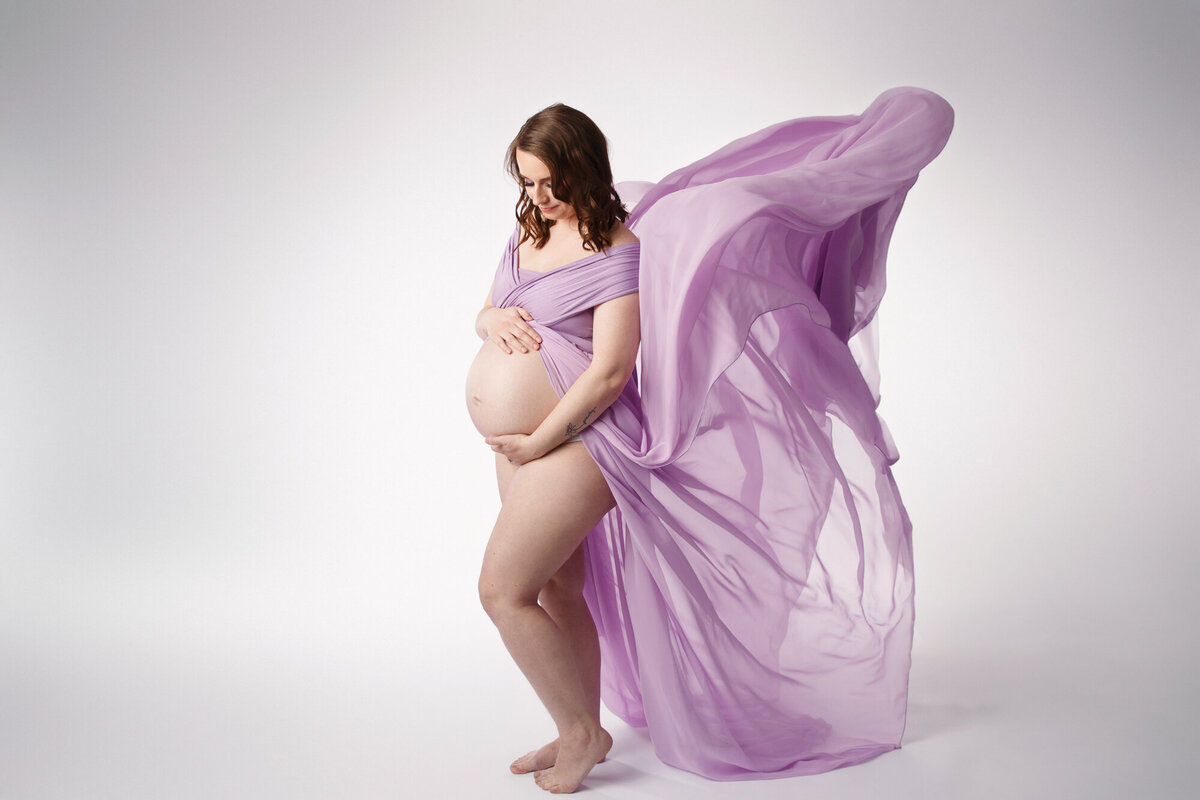 Pregnant woman wearing a purple maternity gown flowing behind her