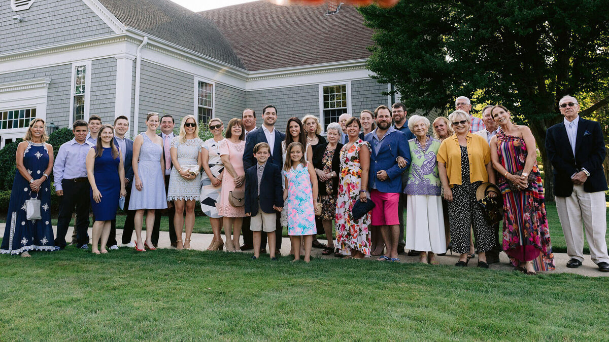 The bride and the groom, together with their families, are in front of a house at Cape Cod, Osterville, MA.