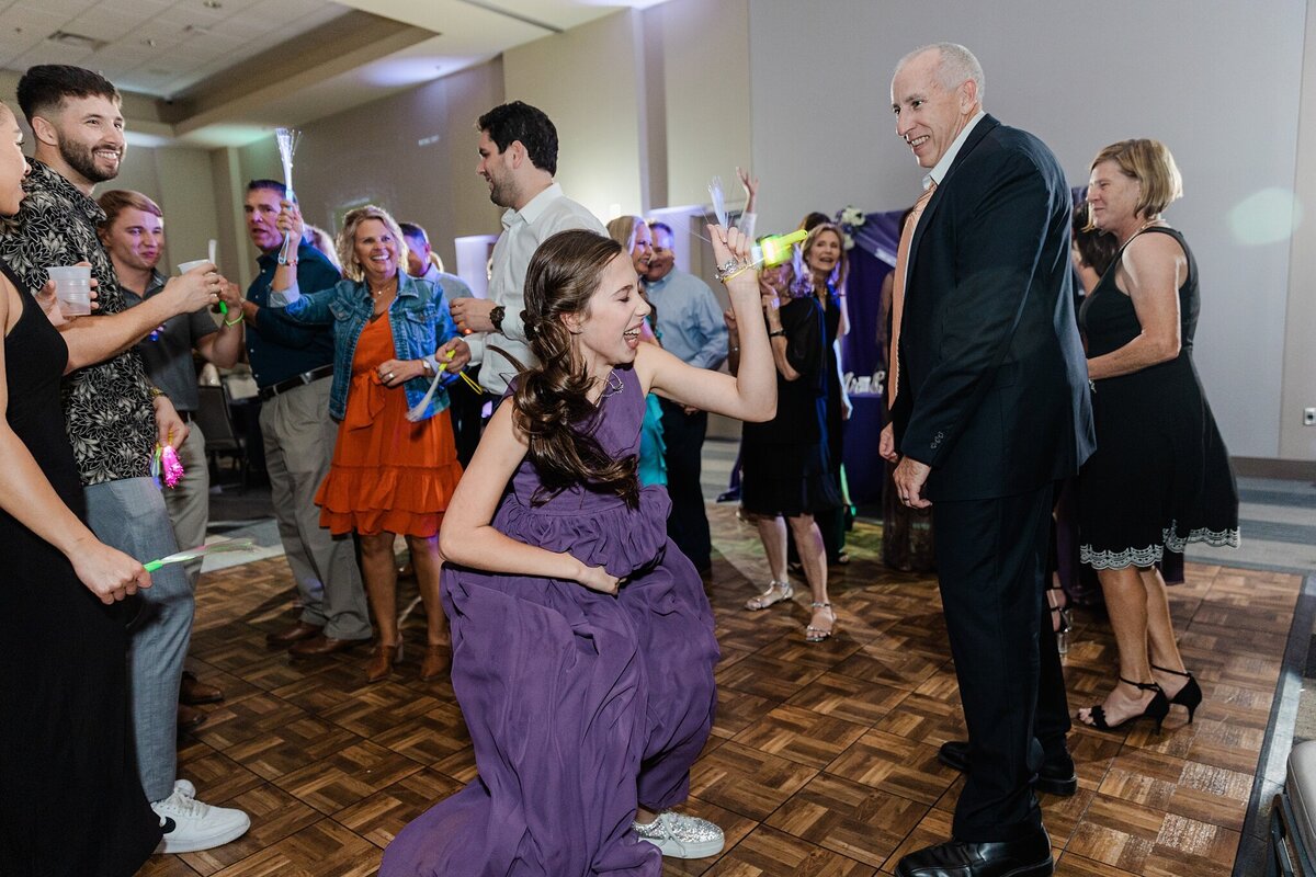An action shot of many wedding guests dancing and celebrating during a wedding reception at the Amon Carter Center at Lena Pope in Fort Worth, Texas. Guests of all ages and varying degrees of dress all share the dance floor and are laughing, dancing, and celebrating together.