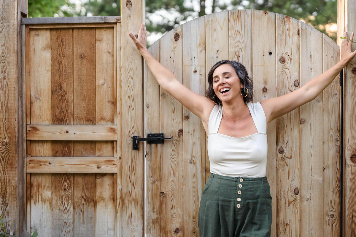 creative headshot of joyful woman in white top against a wooden door outside