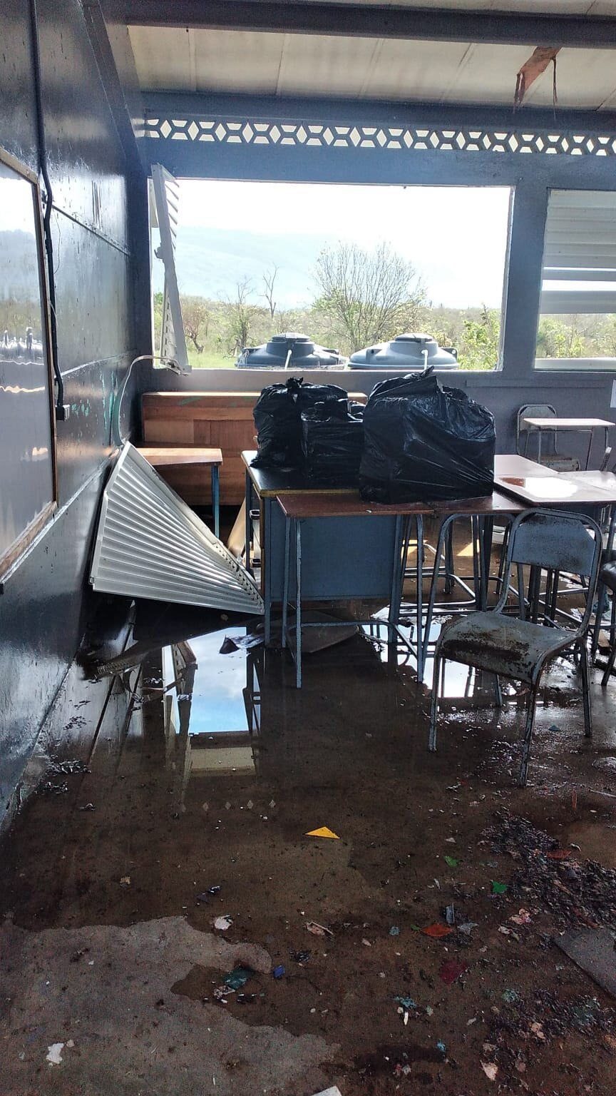 A flooded classroom with overturned desks and water-damaged furniture.