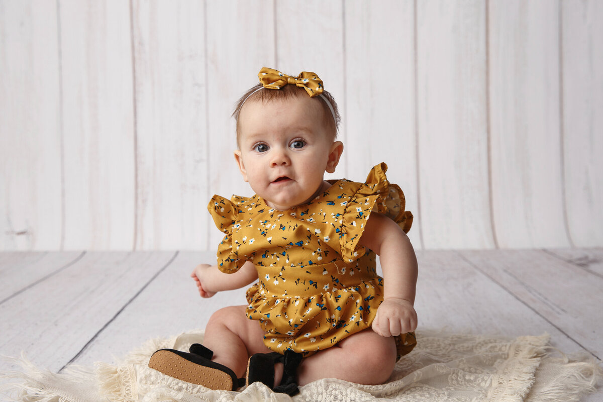 Milestone image of a  six month old girl wearing a yellow print dress.