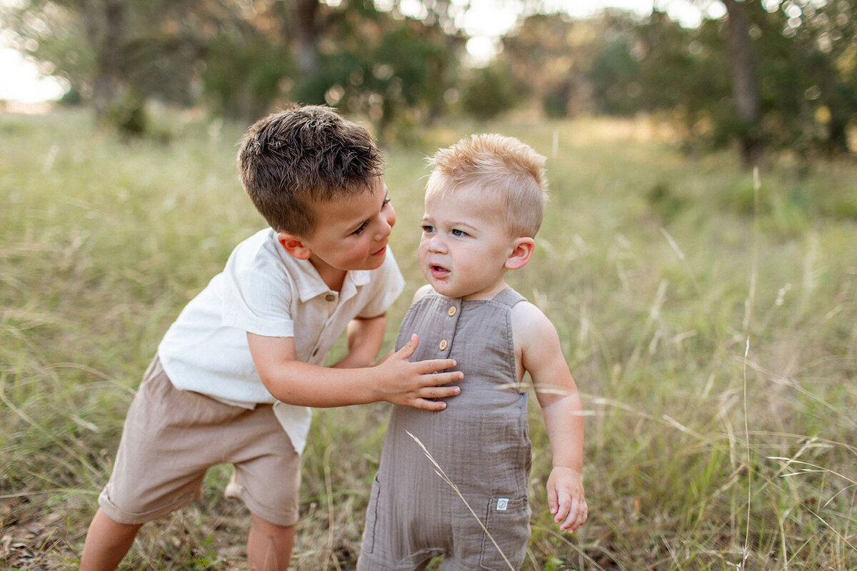 Two children standing together in wildflower field - San Antonio children's photographer Sara James captures sweet sibling moments and childhood memories in natural Texas outdoor setting
