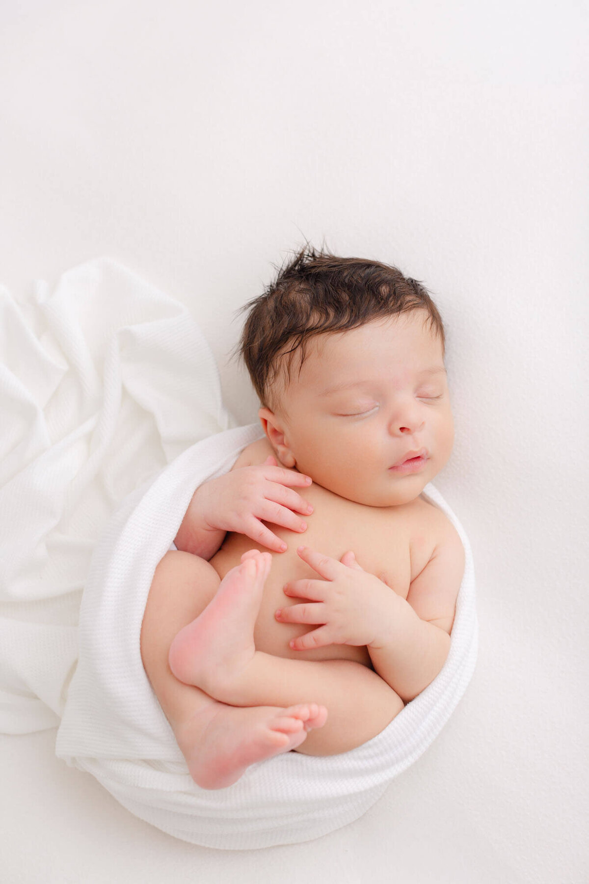 baby swaddled in a white blanket with arms and feet showing laying on a white blanket. Portland Newborn Photography Session