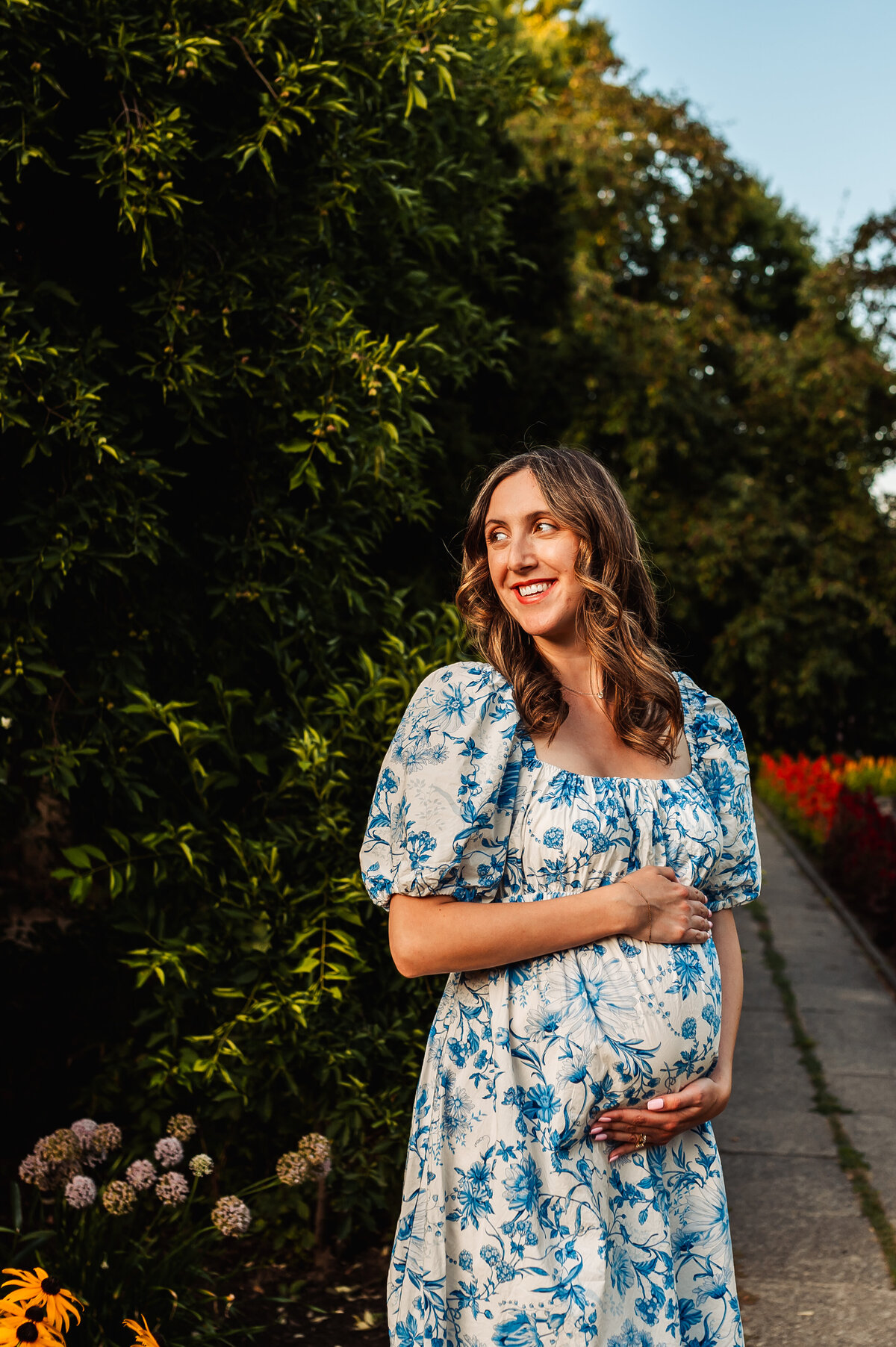 Smiling woman in a floral dress standing among greenery during Ottawa summer mini session.