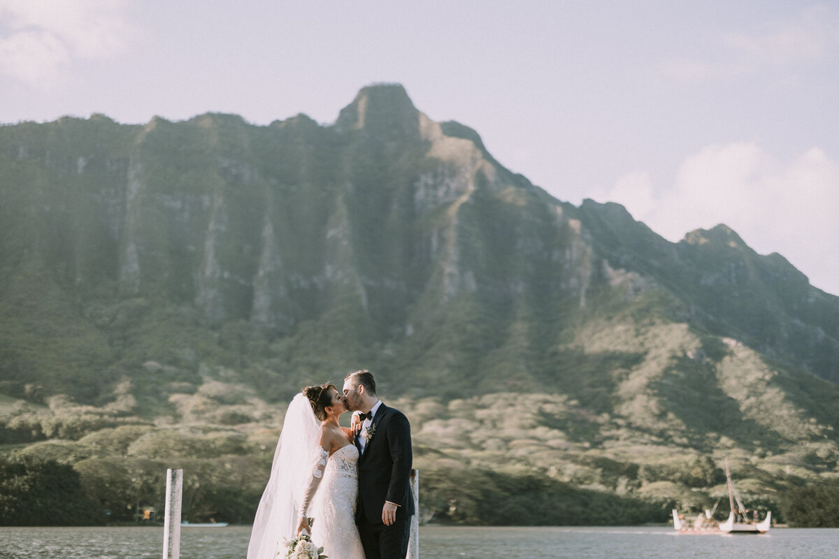 Wedding couple hugging holding wedding bouquet on dock at Kualoa Ranch