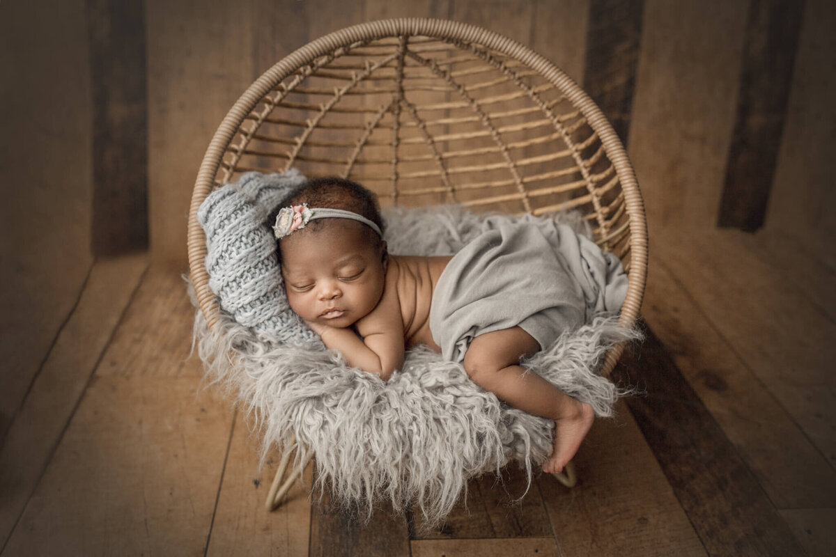 newborn girl posed in bamboo prop on grey rug