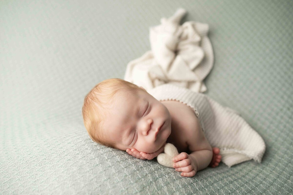Tiny red-haired newborn boy resting on a plush pillow, his hands gently placed near his face