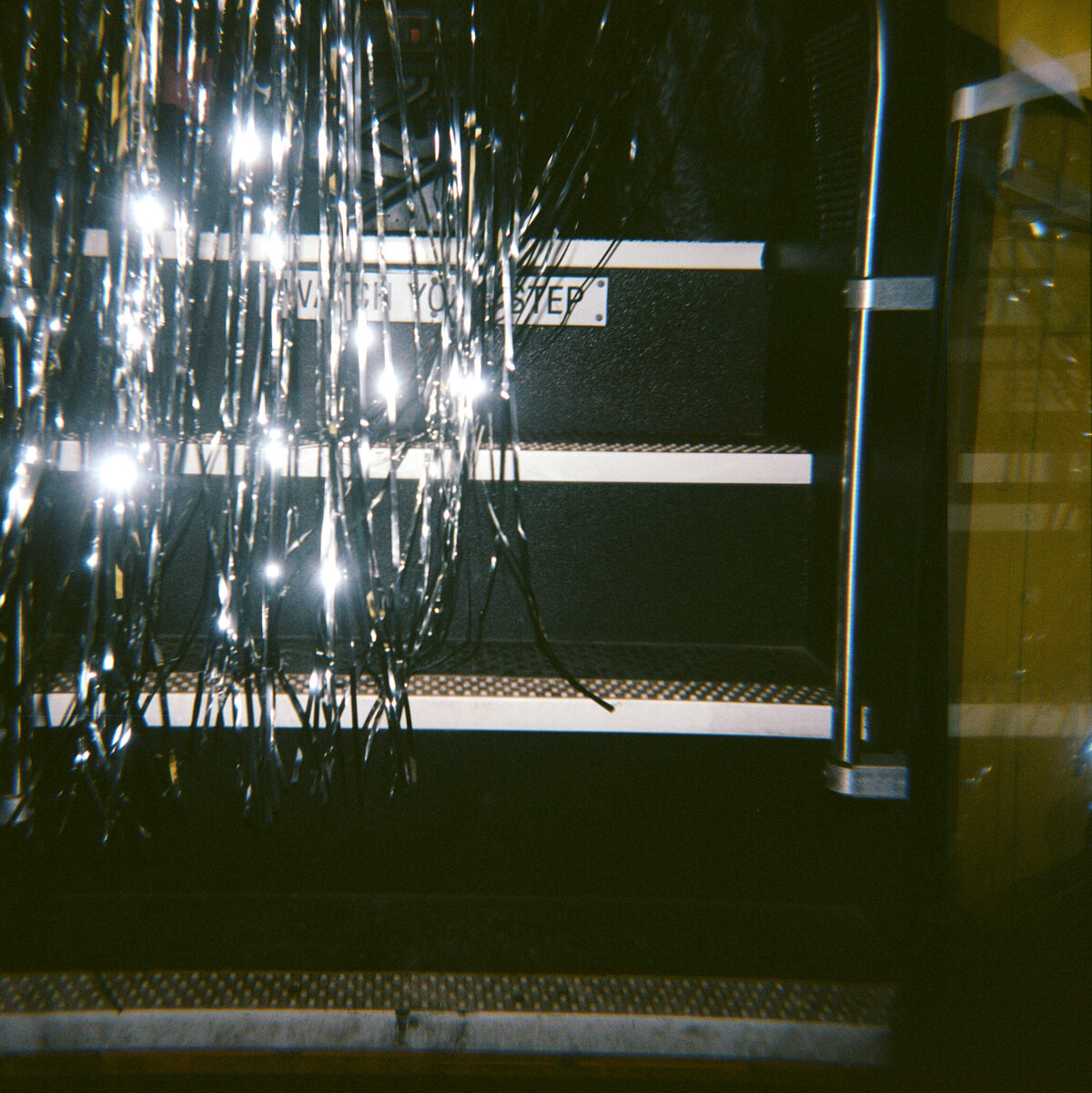 Wedding party bus interior with sparkly tinsel streamers and 'Watch Your Step' sign on stairs, captured in candid aesthetic on 120mm film.