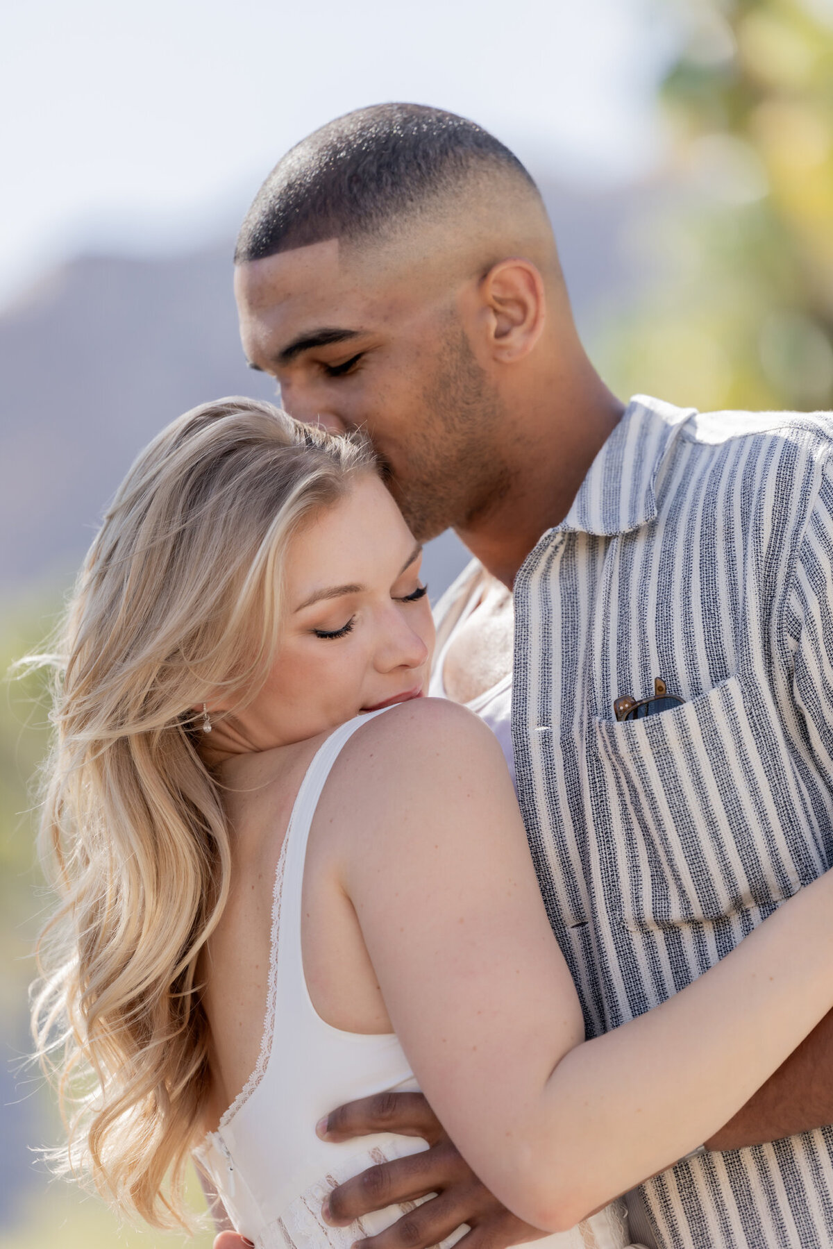 Romantic couple embrace with closed eyes, framed by warm tones and soft sun flare.