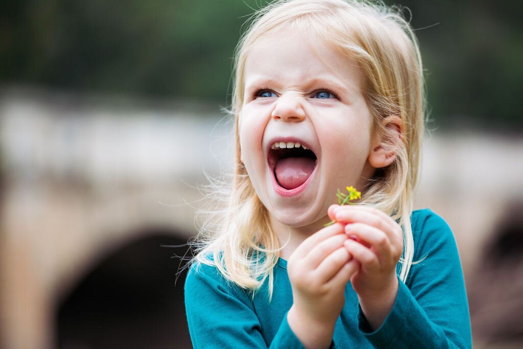 A young girl smiles happily while holding a little yellow flower.