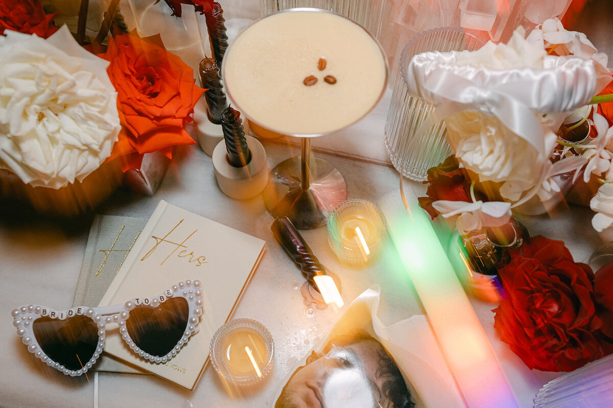 Wedding flat lay featuring vow book, glowing sticks and ring box, styled with red and pink tones
