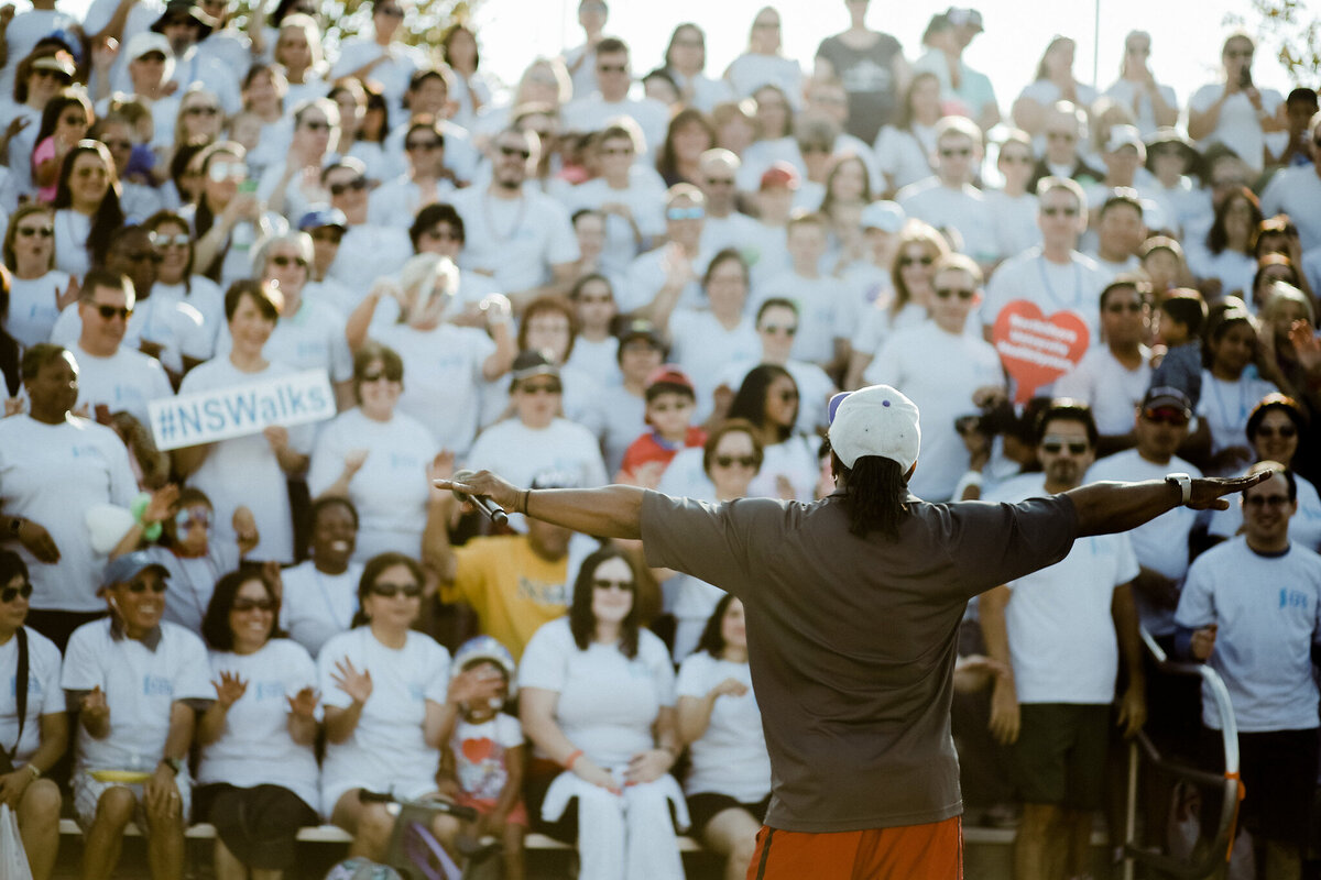Chicago DJ on stage leading a large crowd during a community walk event with #NSWalks participants