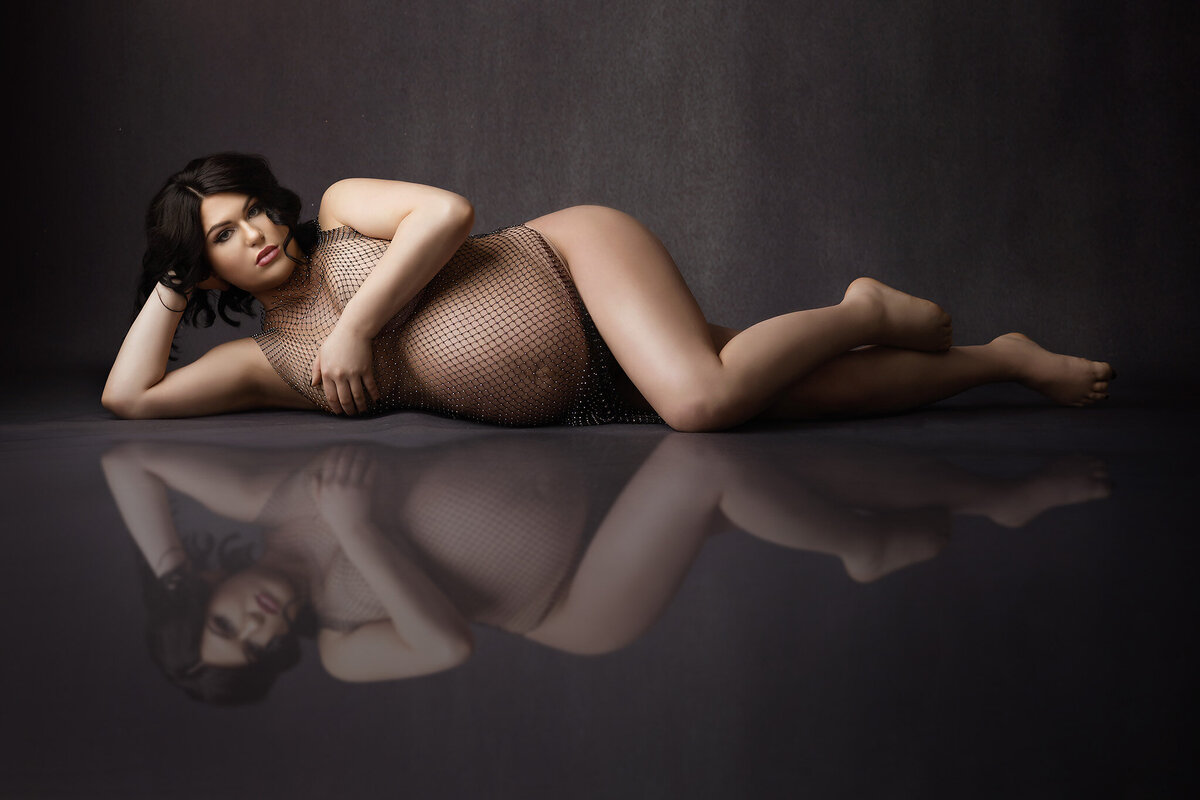 Alluring maternity photo with a woman laying on her side wearing a black fishnet gown with rhinestones. Captured by Dallas maternity photographer Lindsay Walden.