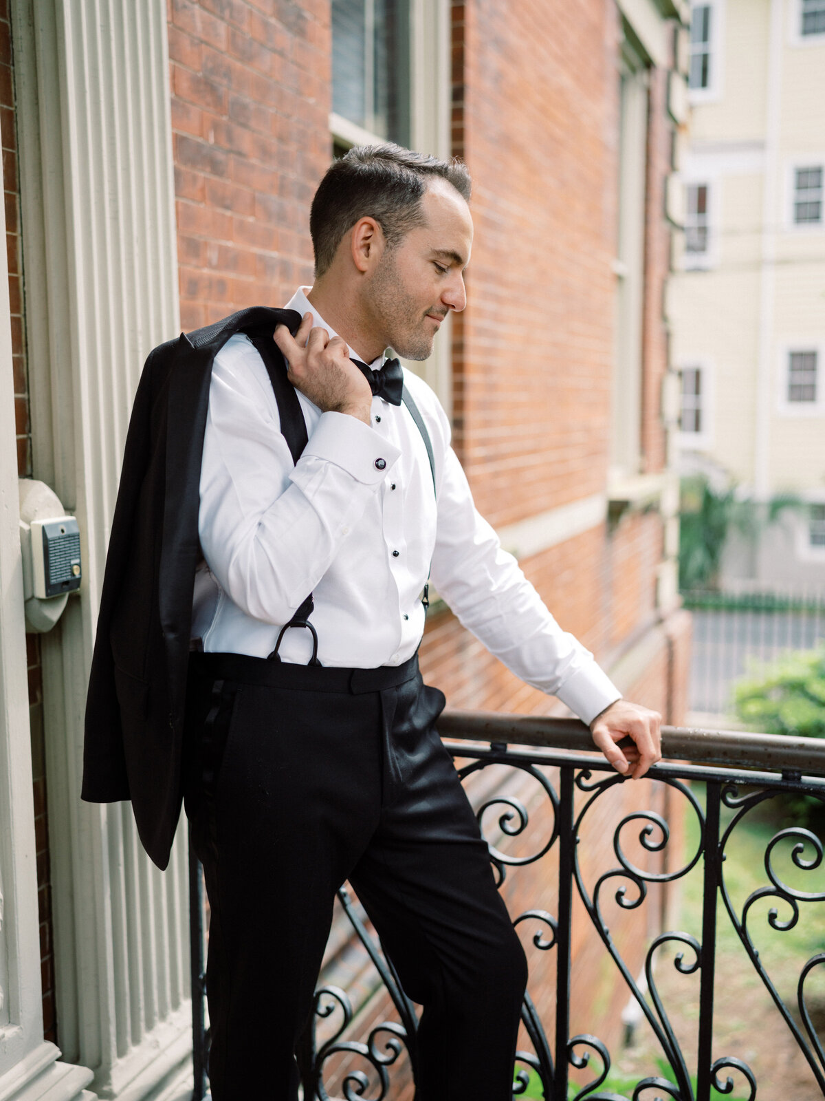 The groom posed elegantly on a balcony, showcasing his stylish tuxedo, reflecting confidence and excitement before the wedding ceremony in a beautiful wedding venue in Charleston.