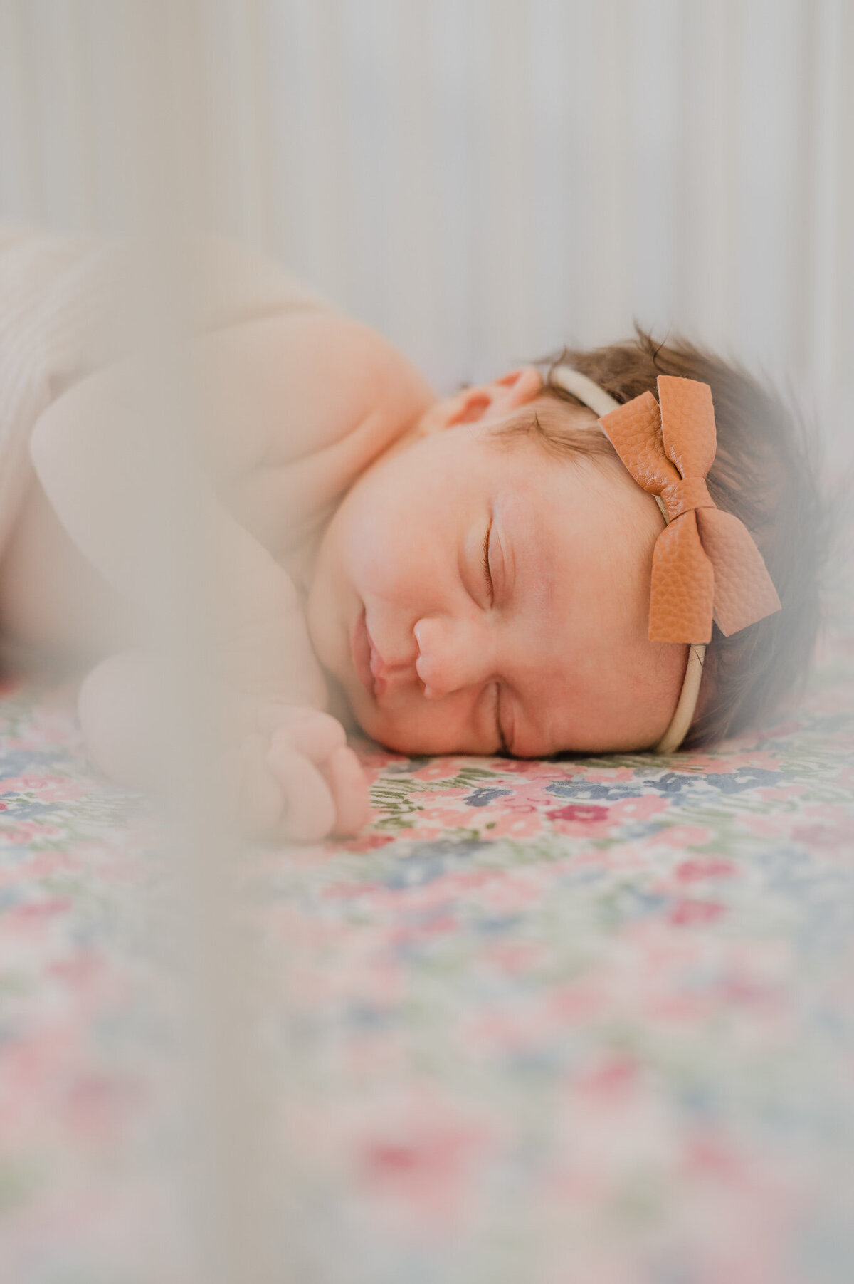 Close-up portrait of a sleeping infant girl in her crib. The image is taken through the rails, which are blurred out.