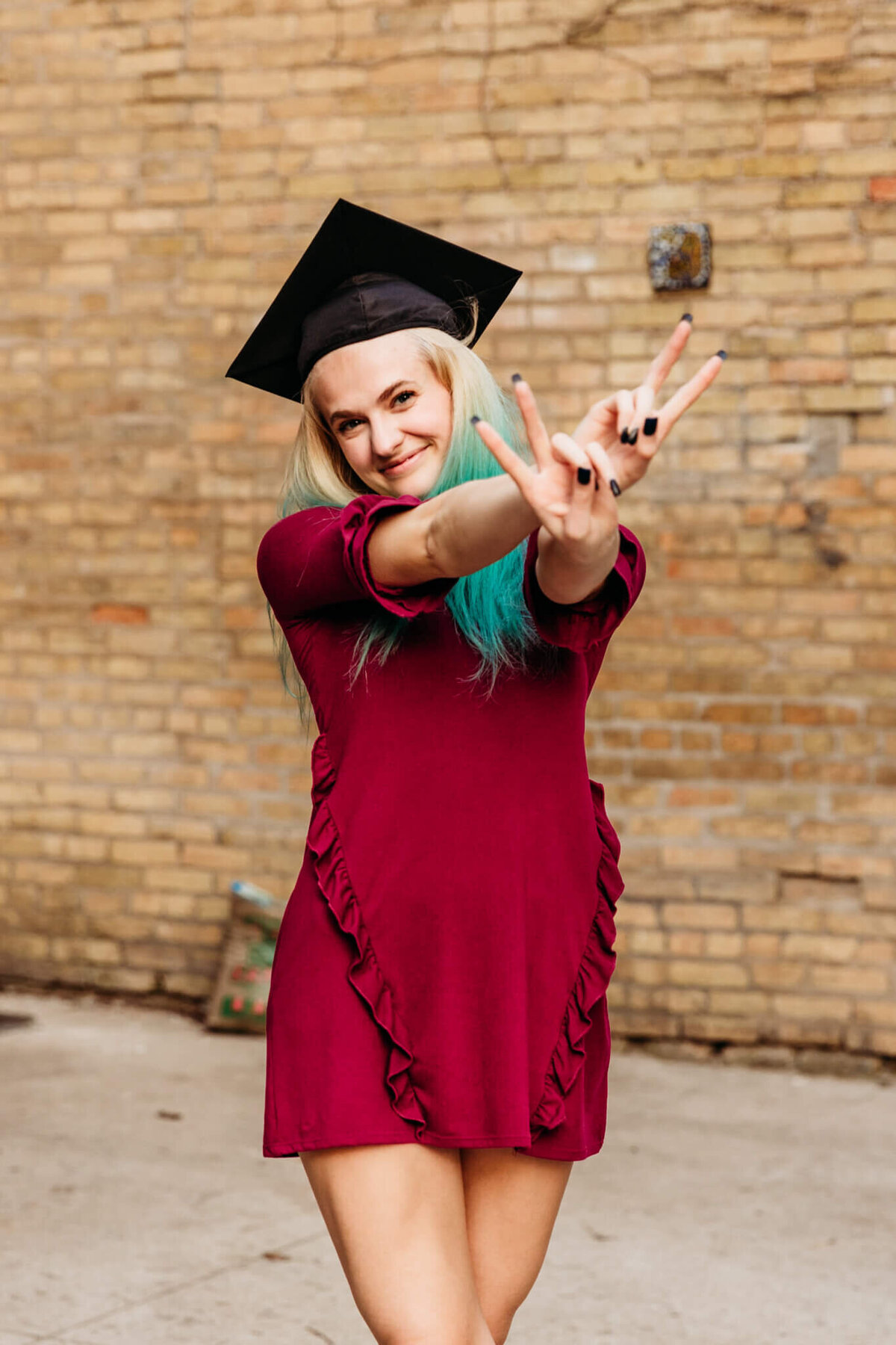 high school graduate holding up two fingers with each hand for cap and gown photo session
